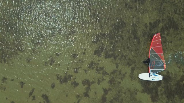 aerial view and rotation of drone camera over a surfer who goes in shallow water and drags a windsurf board with a sail