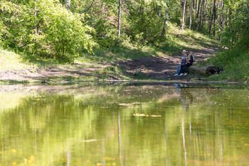 Fototapeta na wymiar A family sits on a log by the pond
