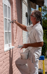 Hampshire, England, UK. 2020. Painter decorator painting small windows on a rural house