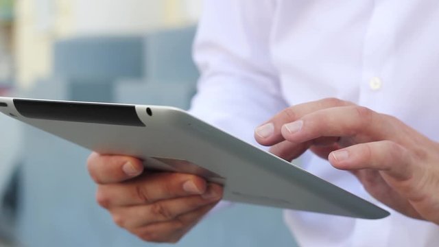 A man in a white shirt and blue jeans raises his hand and looks at the tablett and presses the screen. High quality FullHD footage