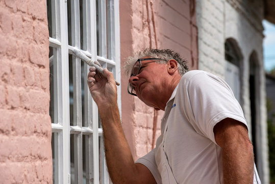 Hampshire, England, UK. 2020. Painter decorator painting small windows on a rural house