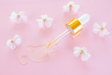 Cosmetic pipette with oil on pink background close-up. Around - white flowers. Stylish concept of organic essences, beauty and health products. Copy space, minimalism, flat lay. Modern apothecary.