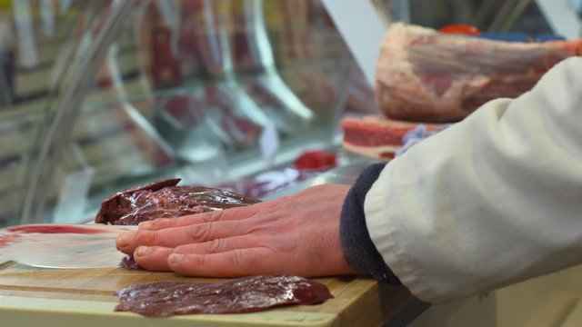 Butcher cuts thin slices of liver meat on chopping board