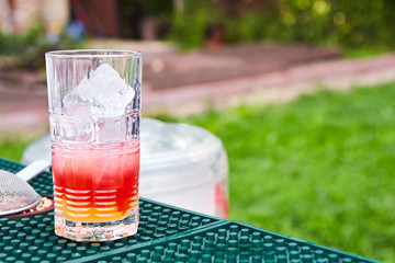 Refreshing summer non alcoholic drink cocktail with ice. Cocktail with ice in a glass with straws. Cocktail with Basil on a green table against the background of nature. Outdoor party
