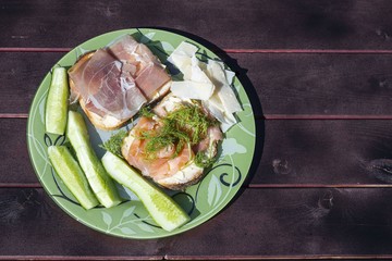 Close up view of plate with two sandwiches, chees and cucumber on wooden background. Healthy eating concept. 