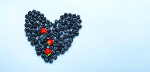Conceptual food. Fresh berries in the shape of heart on blue background. Close-up