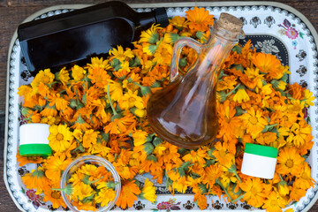 There are many calendula flowers on the tray, there is a bowl, there are two jars of cream and a bottle of oil..