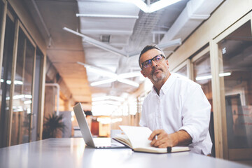 Mature professor of the University is working on a doctoral thesis using contemporary device and notepad. Skilled businessman making plans with respect to its corporate