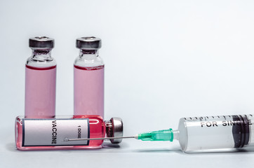 Syringe with a needle and a dose of vaccine inside. Vaccine in glass bottles on a white background.