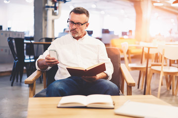 Fototapeta premium Talented male administrative manager making online banking paying for purchases via smartphone connected to free wireless connection in cafe wifi zone during free time enjoying reading books