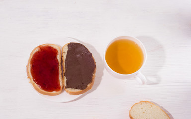 оpen sandwiches with homemade strawberry jam and chocolate nut butter, cup of tea on a white wooden background