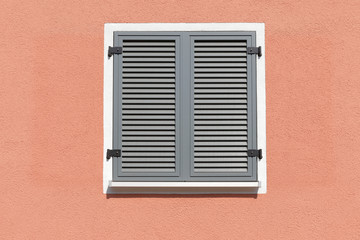 Sunny day with window with shutters on a light red house wall, space for text as a background