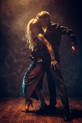 Dance and love concept. Young couple in elegant evening dresses posing in the room filled with dramatic light. Two dancers man and woman holding each other in passionate pose
