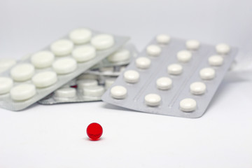 a pile of packs of white pills in the background and one red round pill