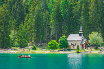 people resting near little church at lake beach in dolomites mountains