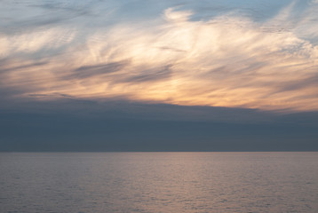 Gray, white and orange clouds on the blue sky above the sea at dawn