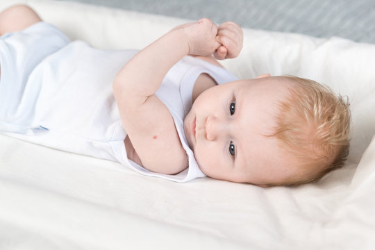 A beautiful newborn in a white bodysuit with traces of BCG vaccination-the TB vaccine-on his arm. The baby is lying on changing table and looks away