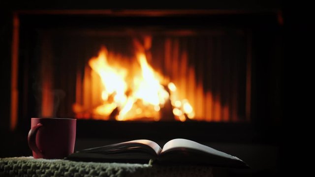A book and a cup of hot haunted on a table near the fireplace. Winter leisure concept