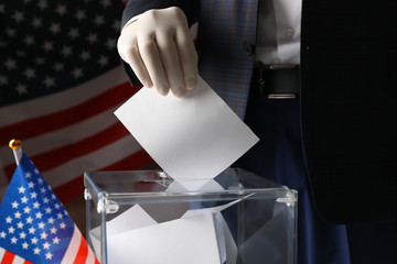 Man in glove putting ballot into voting box against american flag