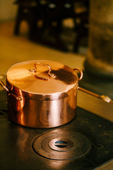 Copper casserole with a closed lid on an antique stove with burners.