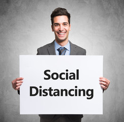 Smiling businessman holding a white board with the text Social Distancing