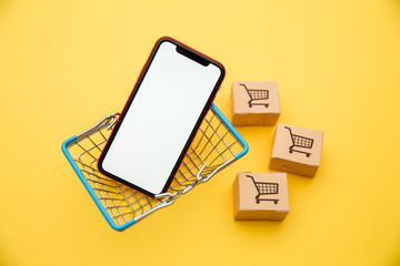 Online shopping concepts with basket, boxes and smartphone on yellow background. Ecommerce market....