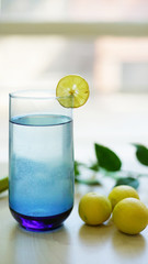 
lemonade in glass on wooden table with lemons, lemon squeeze and branch out of focus background. green background         