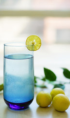 
lemonade in glass on wooden table with lemons, lemon squeeze and branch out of focus background. green background         