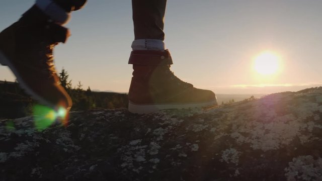 The traveler's feet at the top of the peak, through them shines the rising sun and beautiful landscape in the distance