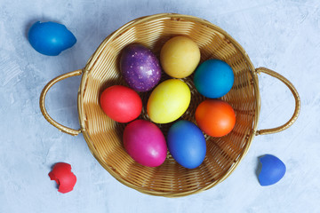 Colorful Easter eggs in a basket on a blue background. Flat lay.