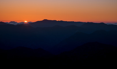 Colourful sunset with orange color and sun at the horizon above the mountains