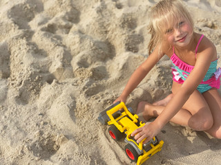 Pretty little girl play with toys on the sandy beach. Summer vacation. Copy space