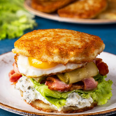 Potato pancakes burger with fried eggs, bacon and salt cucumber. Closeup