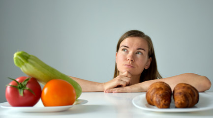 Woman with puzzled sight in choosing between vegetables and dessert. Balanced diet, healthy nutrition, clean eating or weight loss concept. Banner. Copy space.