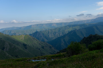 the roadbed is uneven, winding, passes through mountains and cliffs. Clouds are dark, low, with rain. A thick white fog is spreading along the road.
