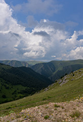 the roadbed is uneven, winding, passes through mountains and cliffs. Clouds are dark, low, with rain. A thick white fog is spreading along the road.