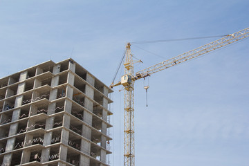 Crane and building construction site against blue sky. Construction of a concrete apartment building. Modern construction