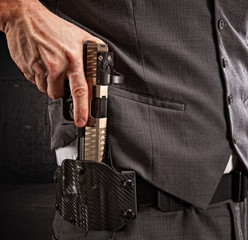 Man drawing his pistol from a holster on his hip, while wearing a vest.