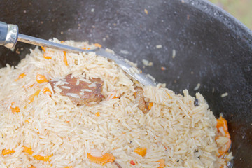 Cooking pilaf in a cauldron on the grill outside in the summer