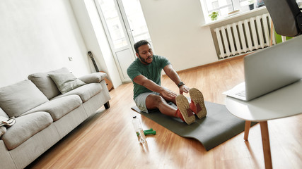 Your coach. Male fitness instructor showing exercises while streaming, broadcasting video lesson on training at home using laptop. Sport, online gym concept