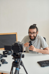 Male technology blogger in glasses looking excited, holding and showing headphones while recording video blog or vlog about new gadgets at home studio