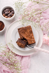 Piece of chocolate nut brownie, on white plate, light textile. Top view, vertical format