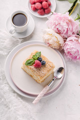 Slice cake of puff pastry with mint, raspberry and blueberry on plate, cup of coffee, peony. Delicate and airy composition, vertical format, top view