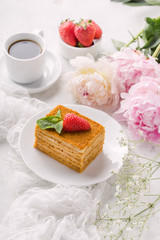 Piece honey multi layer cake, leaf mint, strawberry on plate, cup of coffee and peony. Delicate and airy composition, vertical format.