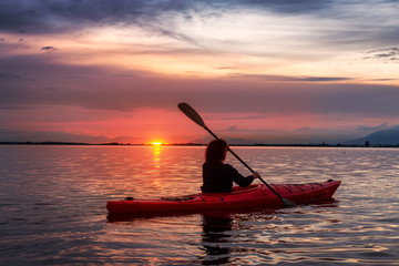 Sea Kayaking in calm waters during a colorful and vibrant sunset. Adventure Girl in Red Kayak. Location: White Rock, Vancouver, British Columbia, Canada.
