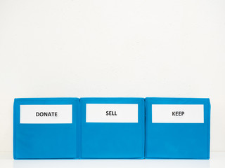 Three Turquoise Bins Labeled Donate, Sell, Keep Against White Wall