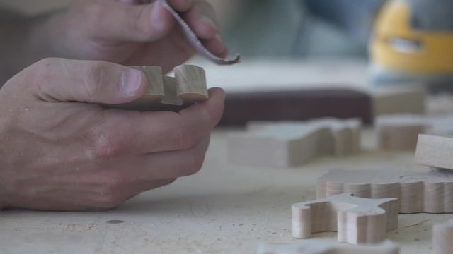 A carpenter polishes eco-friendly wooden toys with sandpaper in his carpentry workshop.