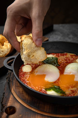 hearty English breakfast - poached eggs, with tomatoes and sauce in a pan on a wooden board
