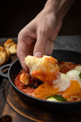 hearty English breakfast - poached eggs, with tomatoes and sauce in a pan on a wooden board
