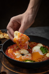 hearty English breakfast - poached eggs, with tomatoes and sauce in a pan on a wooden board
